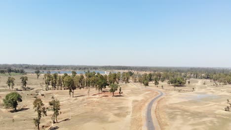 Toma-Aérea-De-Tierra-árida-Con-Carretera-Asfaltada-Y-Agua-A-Distancia-En-La-Aldea-De-Charu-En-Chatra,-Jharkhand,-India