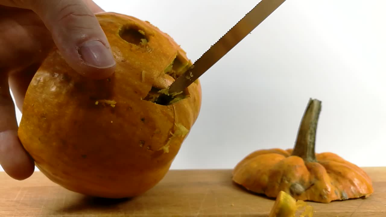 Carving pumpkin part 5, Person carving teeth into Halloween pumpkin with a small pointy serrated knife on wooden chopping board, STILL, ISOLATED
