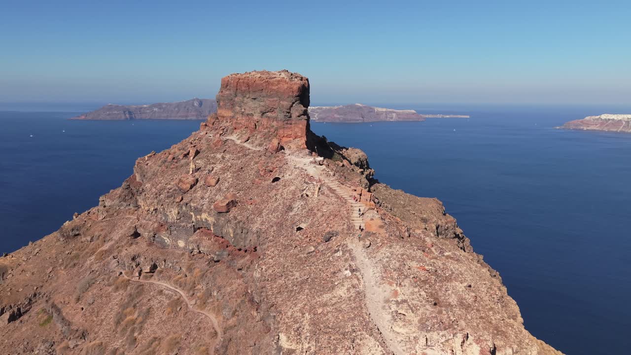 Drone che orbita intorno a Skaros Rock a Santorini con Oia sullo sfondo, catturando le spettacolari scogliere della caldera e l'iconico paesaggio insulare dell'Egeo.