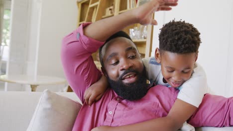happy african american father and son sitting on sofa and embracing, in slow motion