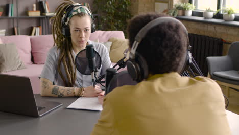 Woman-Sitting-At-A-Table-With-Microphones-And-Computer-While-Recording-A-Podcast-With-Man