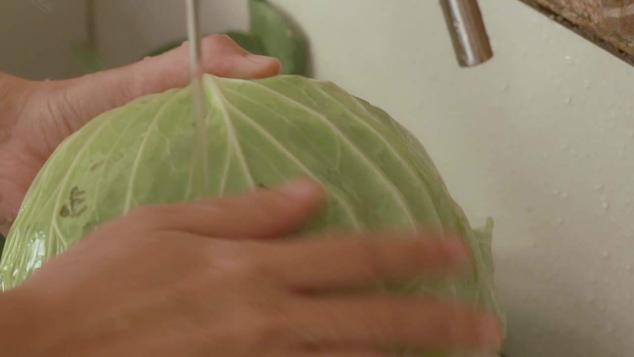 Close up of hands washing cabbage in running water at the kitchen sink showing a candid moment slow living and daily life at home