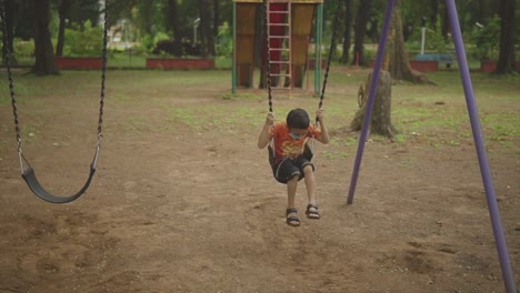 niño indio sentado en el columpio en el parque de la ciudad