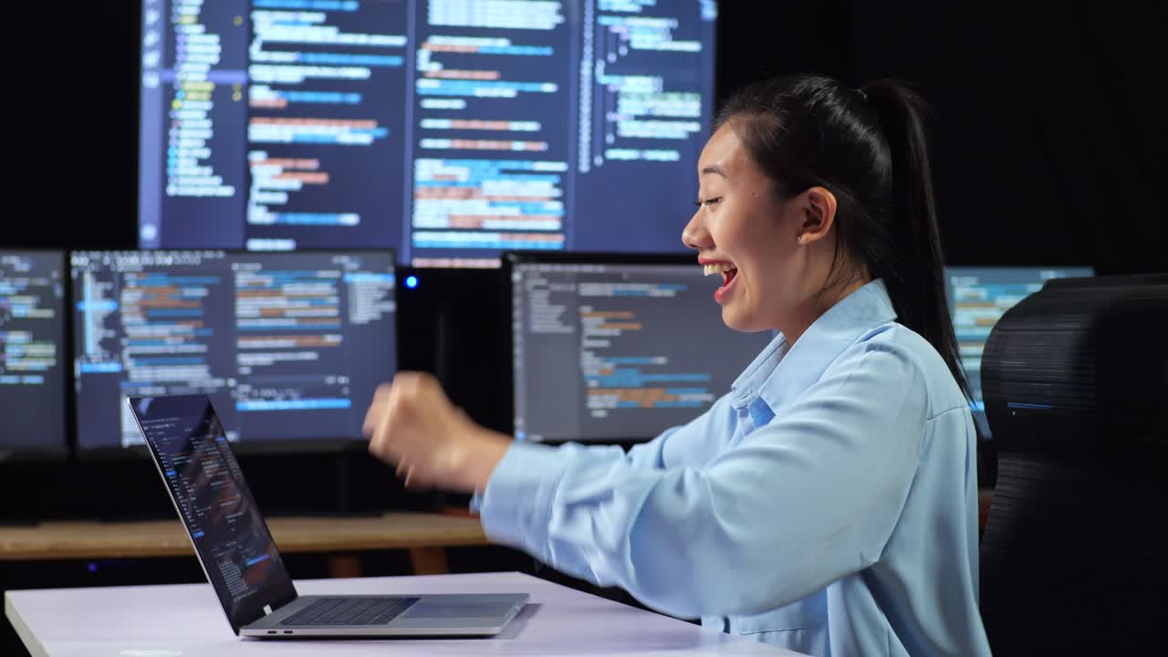 다중 모니터를 사용하여 노트북으로 코드를 작성하는 성공을 축하하는 아시아 여성 프로그래머의 측면 뷰 사무실의 터미널 윈도우 데스크에서 데이터베이스를 보여줍니다.