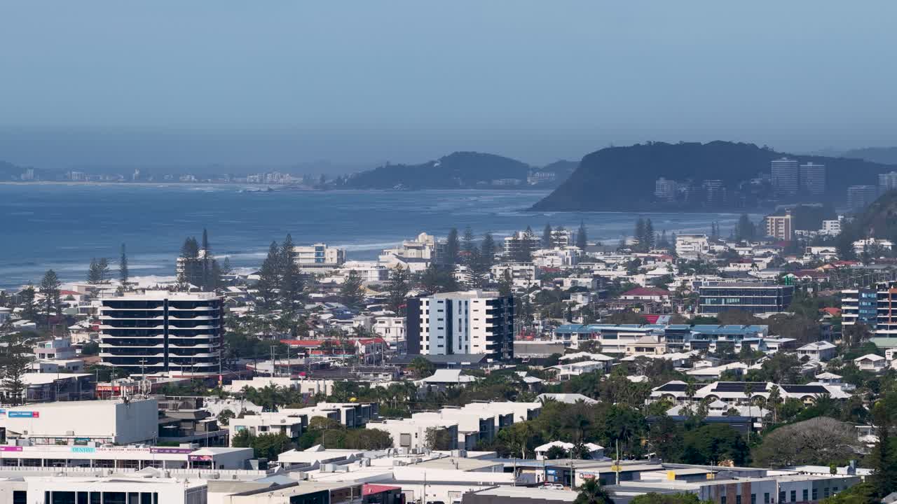 Telephoto drone captures expansive Gold Coast cityscape with ocean backdrop, highlighting urban density and coastal beauty under clear skies