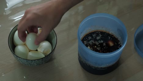 hand adding boiled eggs on marinade soy sauce with sesame seeds. - closeup shot