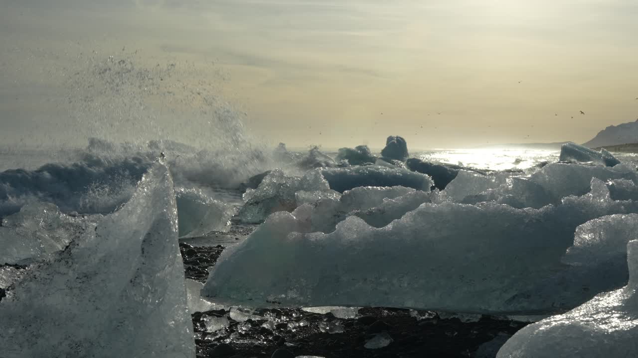 Large ice blocks on black sand beach with crashing waves and golden sunset at Diamond Beach, Iceland