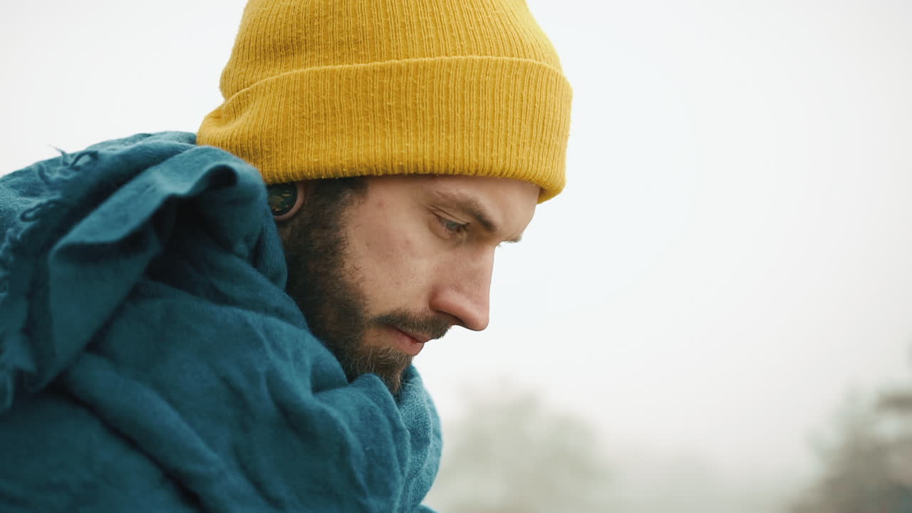 Man with beard and yellow hat looking down in fog