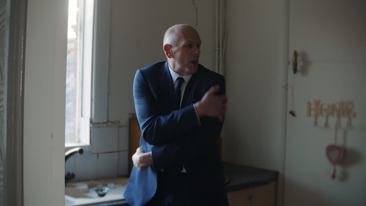 En forvirret moden ældre forretningsmand fryser i et mørkt køkken om vinteren