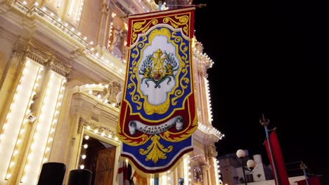 Malta,-Sliema,-religious-flag-hanging-in-front-of-a-decorated-church-at-night