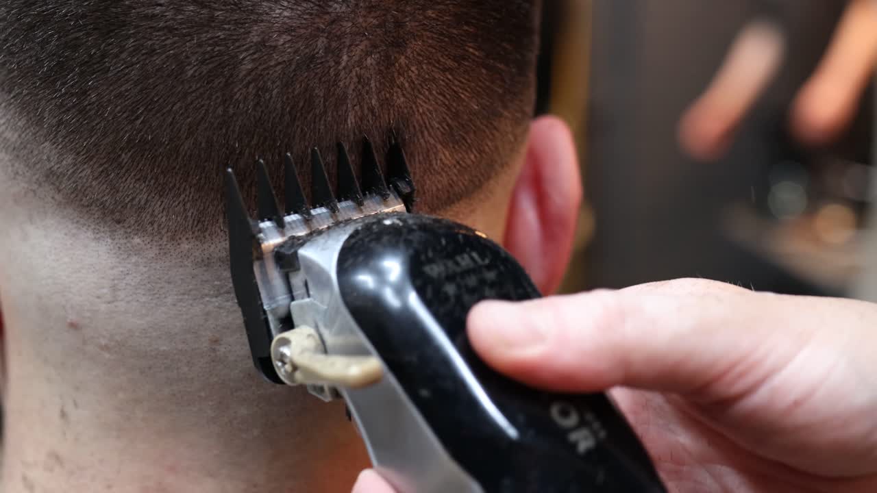 fotografía de cerca de un barbero recortando el cabello de un cliente masculino con cortadoras de cabello mientras trabajaba en una barbería