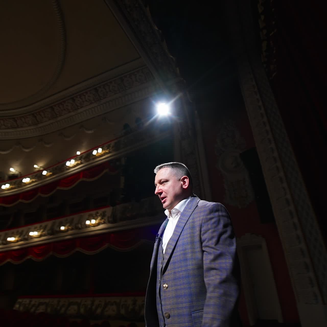Senior male entertainer dances on stage in front of theater hall. Speaker akes audience laugh. Entertainment concept