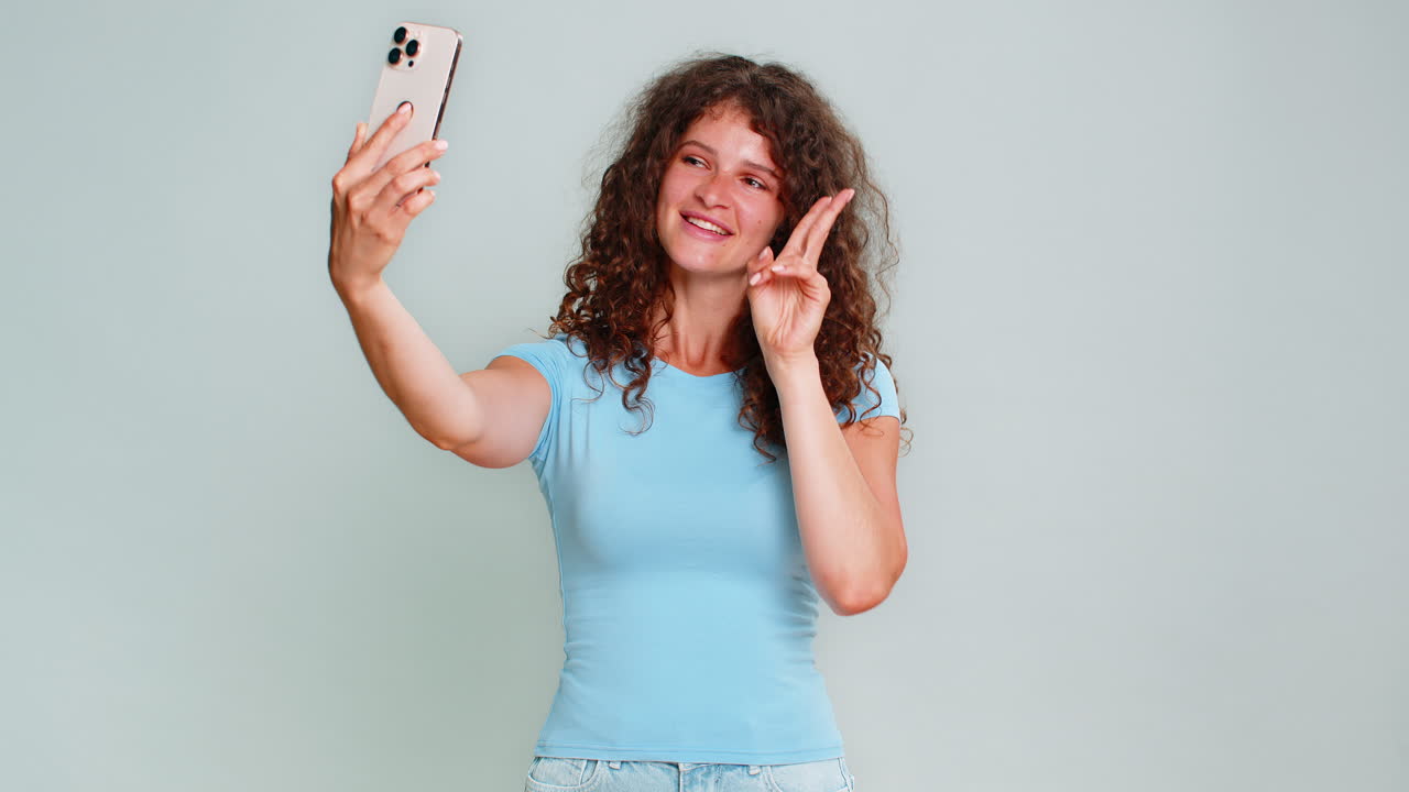 Young woman smiling carefree mood taking selfie photo on smartphone showing peace gesture hand sign