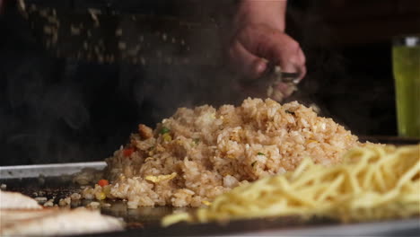 japanese chef prepares fried rice and noodles on a flat top teppanyaki grill