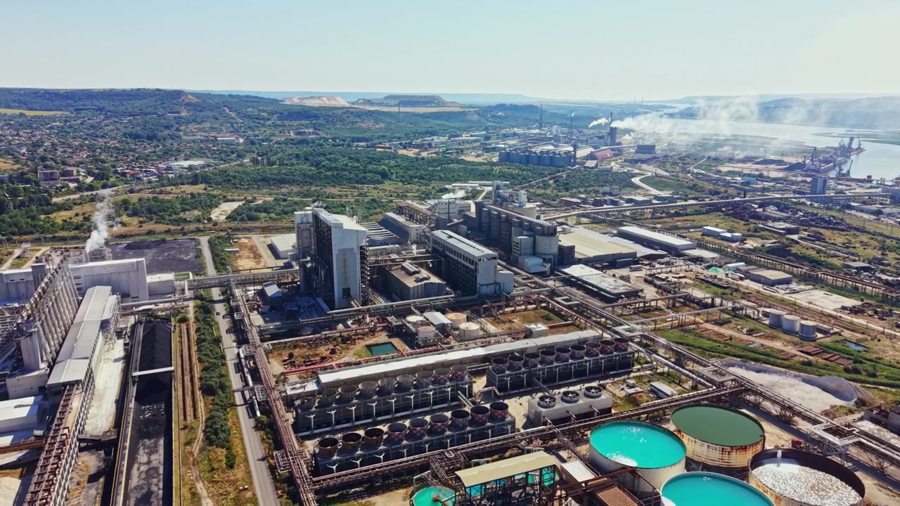 Complejo industrial con tanques de agua y humo a lo largo del río cerca de colinas verdes a la luz del día