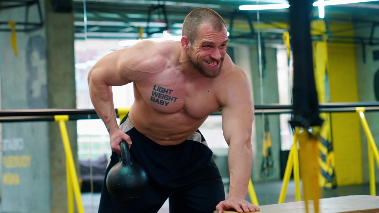 Uomo muscoloso che esegue rematore con kettlebell in palestra