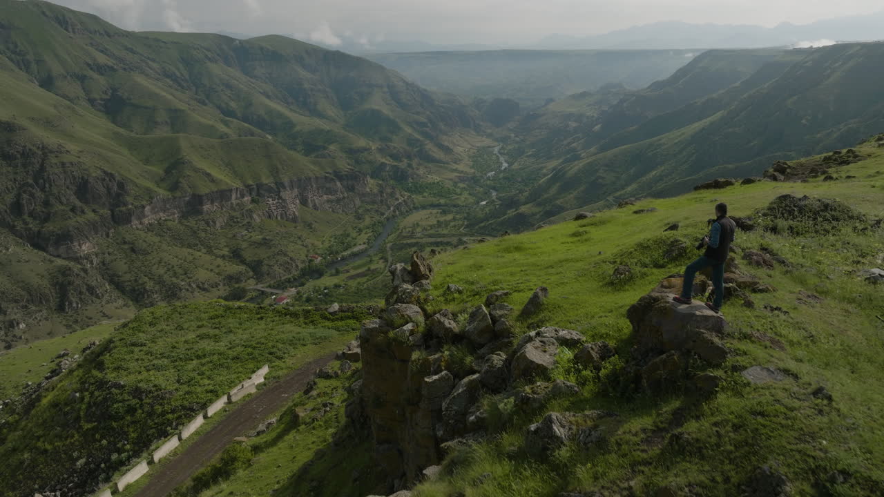 retroceso aéreo que revela a un fotógrafo de la naturaleza que captura montañas y ríos desde un terreno irregular en georgia