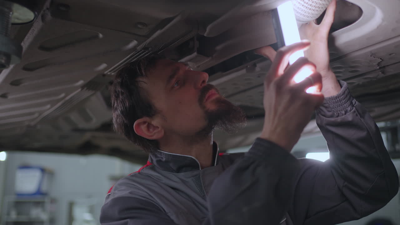 hombre mecánico automático mira debajo del coche levantado en el ascensor en busca de fallas en cámara lenta