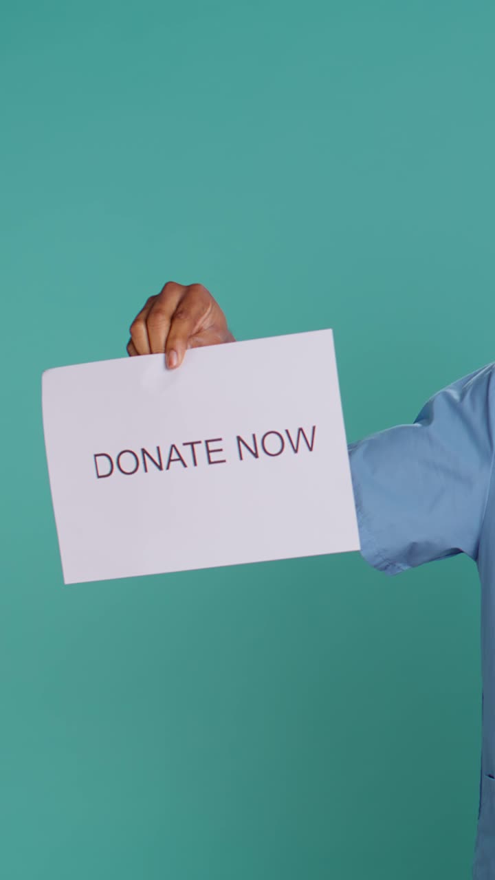 Person Holding 'Donate Now' Sign Against Teal Background