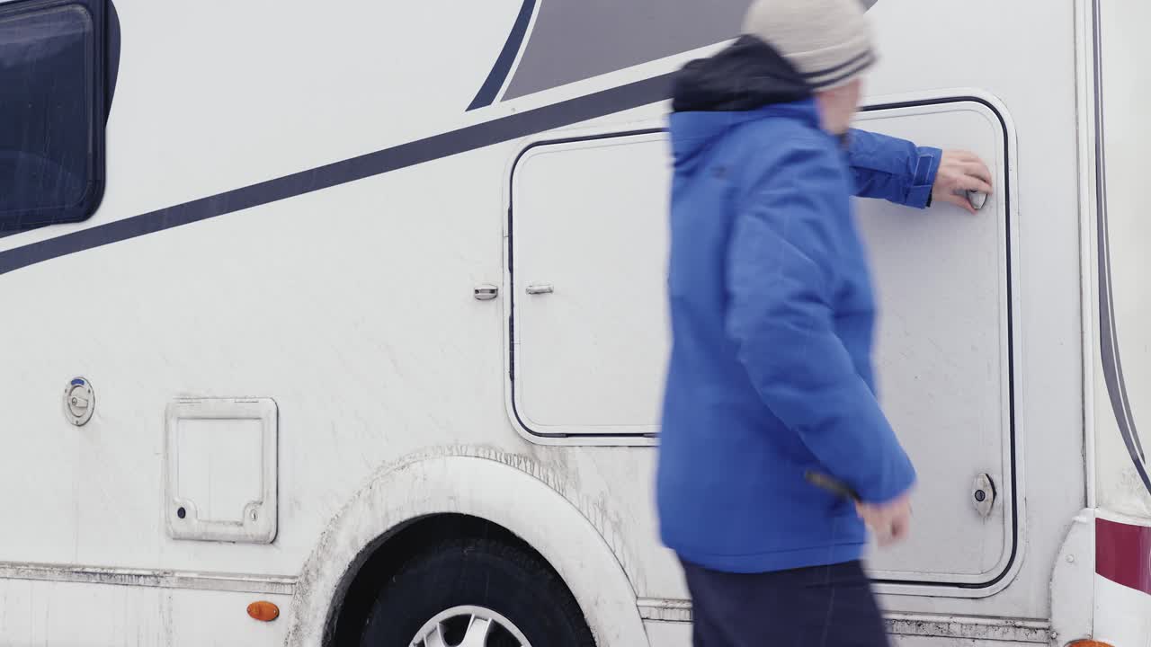 파란 재 ⁇ 을 입은 사람이 겨울 모험 중에  ⁇  진 ⁇  카라반의 측면 화물 문을 열고 있습니다.