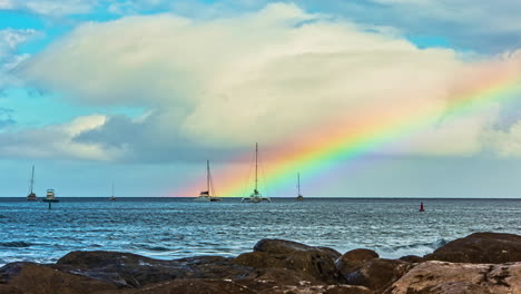 time lapse shot of pacific ocean with anchored sailing boats and rainbow in background - sun reflection after with water surface - clouds moving at sky - hawaii,maui