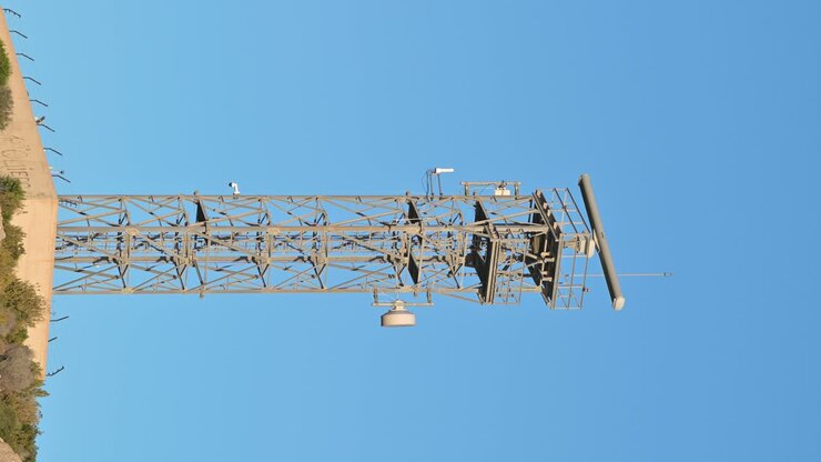Video ravvicinato verticale in tempo reale di un radar marittimo rotante su una base di cemento, sullo sfondo del cielo blu.