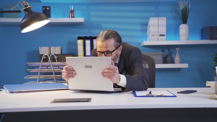 Mature businessman working on laptop rejoicing and smiling with energy.
