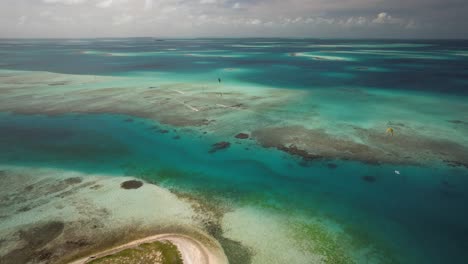 Türkisfarbenes-Wasser-Und-Korallenriffe-Mit-Gleitenden-Kitesurfern,-Luftaufnahme