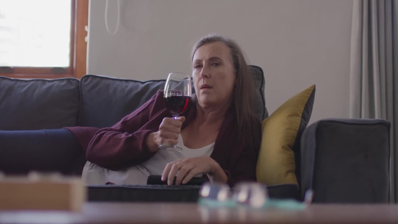 Woman watching TV and drinking wine while laying on the couch at home