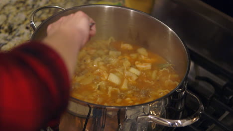 Vista-De-Cerca-De-Arriba-Hacia-Abajo-De-Una-Mujer-Revolviendo-Una-Olla-De-Ciopini-En-Su-Cocina