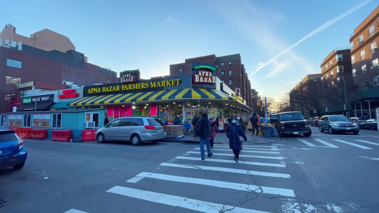 Nowy Jork, USA, 9 marca 2022: Witryna sklepu Apna Bazar na rogu ulicy w Queens. Szeroki widok z narożnika ulicy na fasadę targu rolniczego Apna Bazar, przejście dla pieszych, pieszych, pojazdy, błękitne niebo.