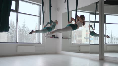 dos jóvenes mujeres yogi practicando yoga aéreo en hamacas verdes en un club de fitness. hermosas mujeres trabajando en clase realizando aero yoga. variación de la postura de la pirámide parsvottanasana