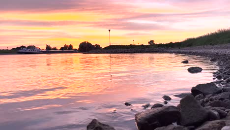 Dramatic-sunset-sun-rays-over-river-IJssel-with-silhouetted-trees-of-vibrant-intense-color-sunset-sky-with-texture-and-detail-of-cloud-cover-lighting-up-orange,-red-and-magenta-tones