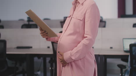 portrait of a smiling pregnant woman holding documents and smiling at camera in the office