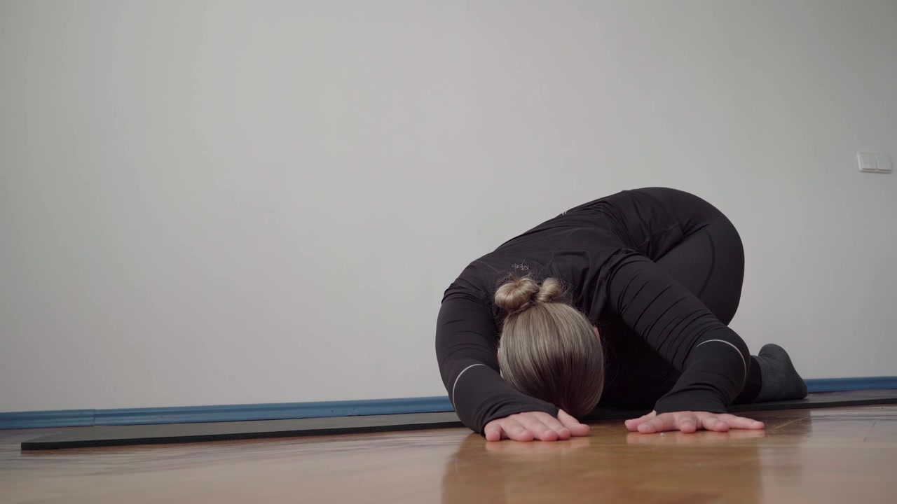 Woman in black sportswear holds child’s pose on a mat, stretching her spine and hips for lower back pain relief and recovery.