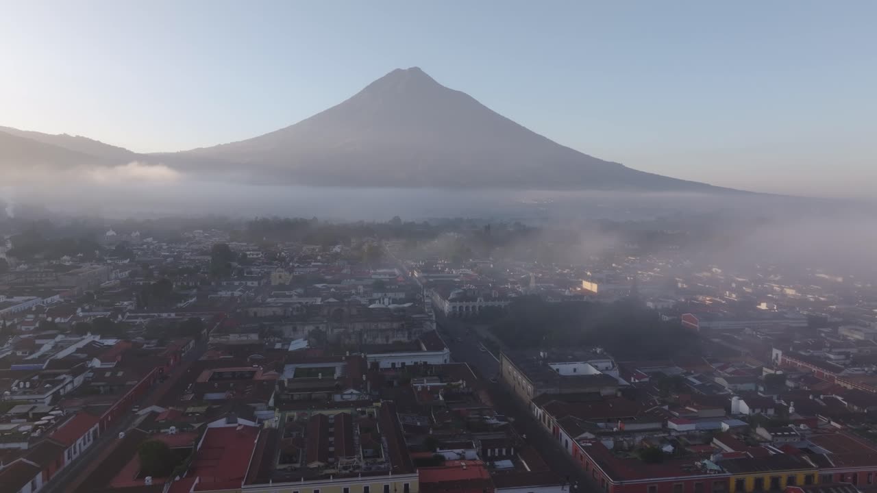 Luftfoto af koloniale Antigua Guatemala under bløde tågede solopgangsforhold med den imponerende Volcán Agua i det fjerne