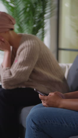 vertical video of upset young woman patient wearing headscarf with head in hands after receiving chemotherapy treatment for breast cancer in hospital clinic