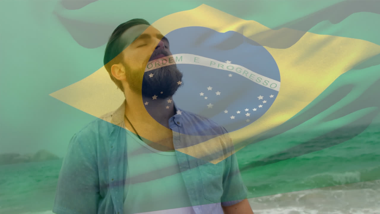 Video compuesto de bandera de Brasil ondeando sobre hombre caucásico con ojos cerrados de pie en la playa