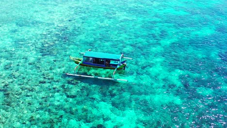 Traditional,-outrigger-passenger-boat-floating-in-the-crystal-clear-turquoise-seawater-near-the-popular-tourist-beach-in-Bali,-Indonesia