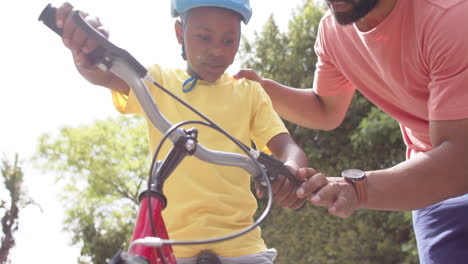 padre afroamericano enseñando a su hijo a montar en bicicleta en un jardín soleado, cámara lenta