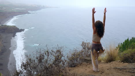 Junto-Al-Océano,-La-Playa-Y-Las-Montañas-Rocosas,-La-Postura-De-Guerrera-De-Yoga-De-Una-Mujer-Se-Convierte-En-Un-Símbolo-De-Motivación,-Inspiración-Y-Búsqueda-De-Un-Estilo-De-Vida-Consciente-De-La-Salud.