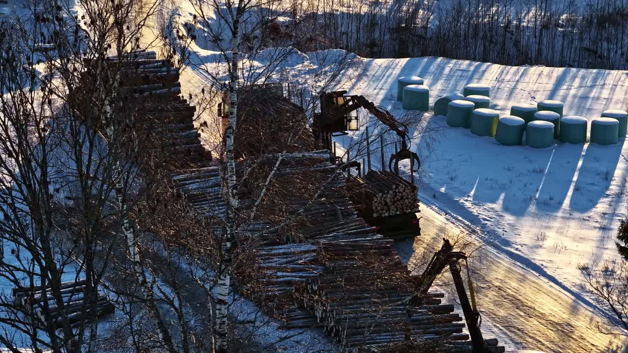 Widok z lotu ptaka na skład drewna, gdzie bale są rozładowywane i układane w stosy.