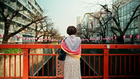 woman on bridge in japanese city during cherry blossom season