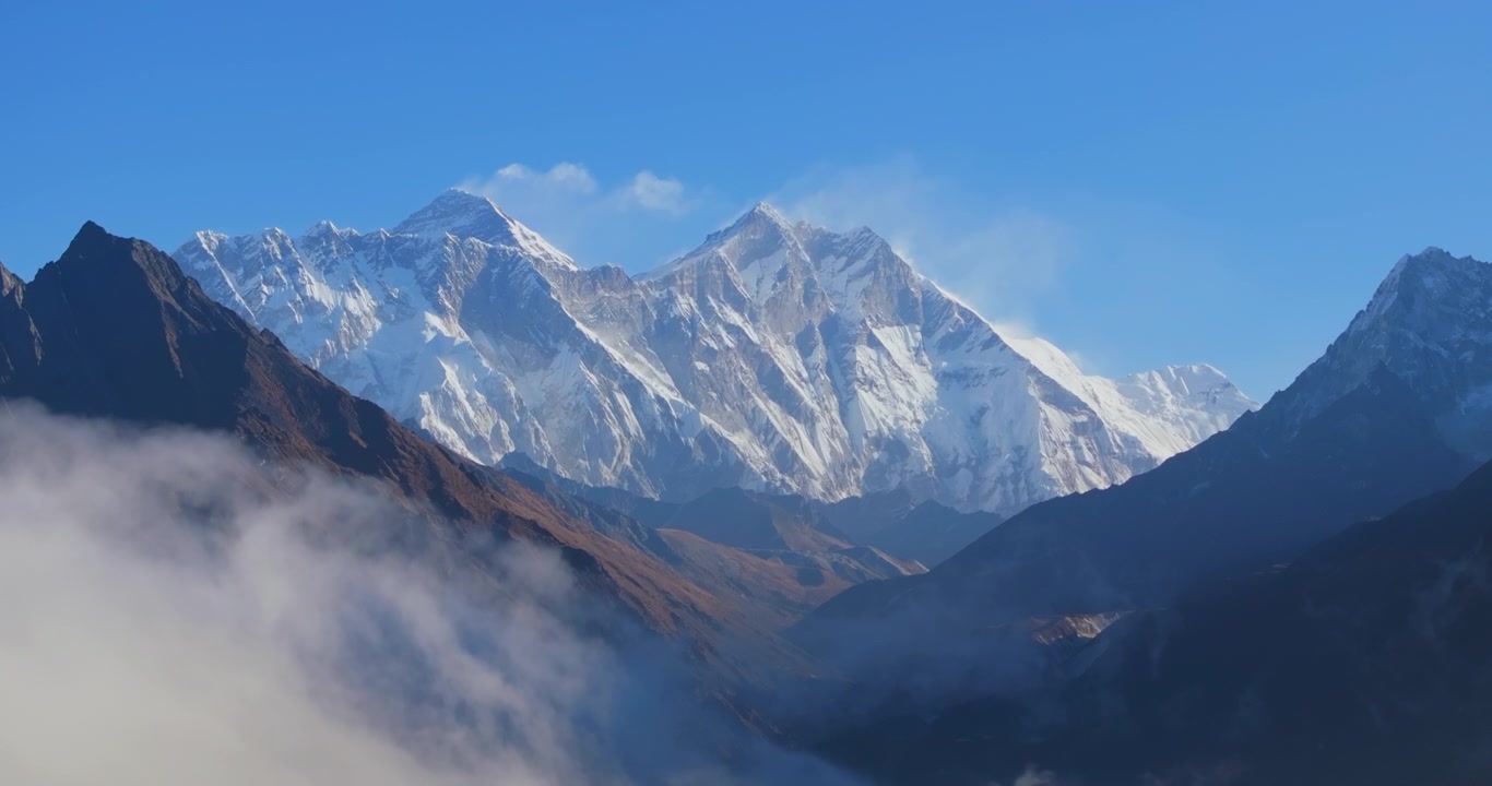 Everest region, Nepal. Tilt-up drone shot emerging from valley clouds to show snow-capped Mount Everest and Lhotse peaks under a blue sky