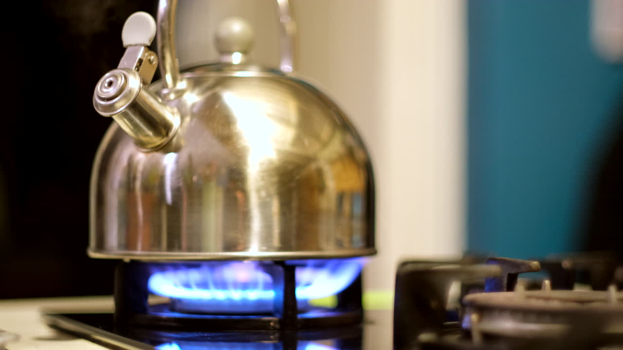 Shiny stainless steel kettle boiling on gas stove burning with blue flame