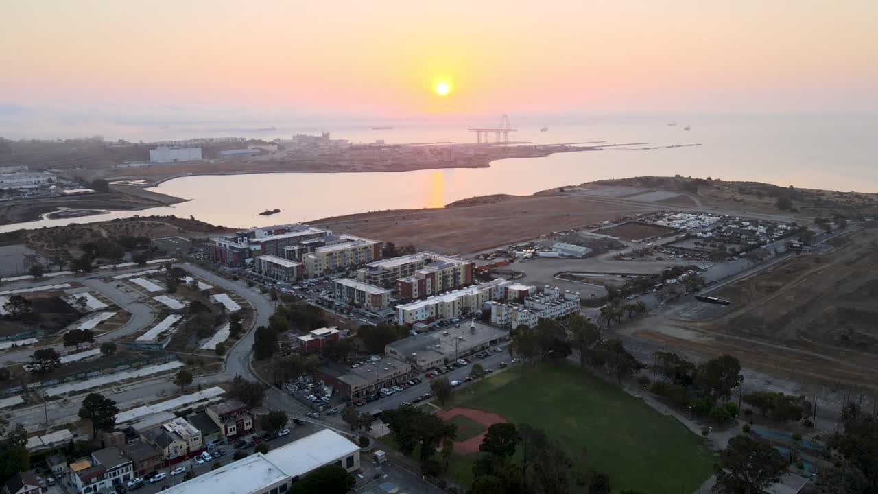 Sliding tilt drone shot revealing a muted sunrise over cargo cranes in Bayview, San Francisco, the bay's waters reflecting the gentle light