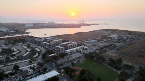 Sliding-tilt-drone-shot-revealing-a-muted-sunrise-over-cargo-cranes-in-Bayview,-San-Francisco,-the-bay's-waters-reflecting-the-gentle-light