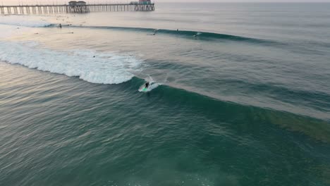 Impresionante-Toma-Aérea-De-4k-De-Un-Surfista-Atrapando-Una-Ola-Al-Amanecer-En-La-Soleada-Ciudad-De-Surf,-EE.UU.,-California