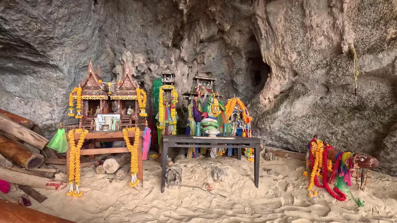 Walking handheld POV towards a Hindu animist shrine decorated with offerings and phallic symbol called lingams in Phra Nang Cave or Princess Cave, authentic local thai folklore. Krabi, Thailand