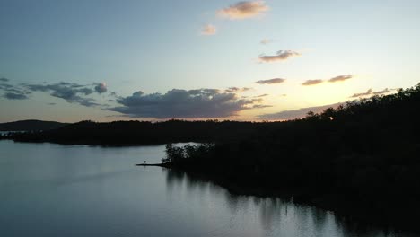 Ascending-drone-shot-flying-over-Wivenhoe-Dam-Lake,-Camera-Facing-Sun-at-sunset